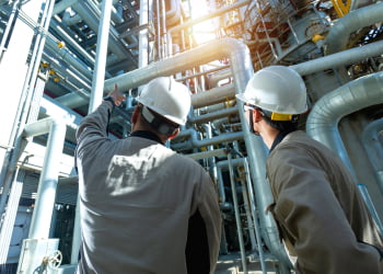 Dois homens olhando e apontando para tubos industriais.